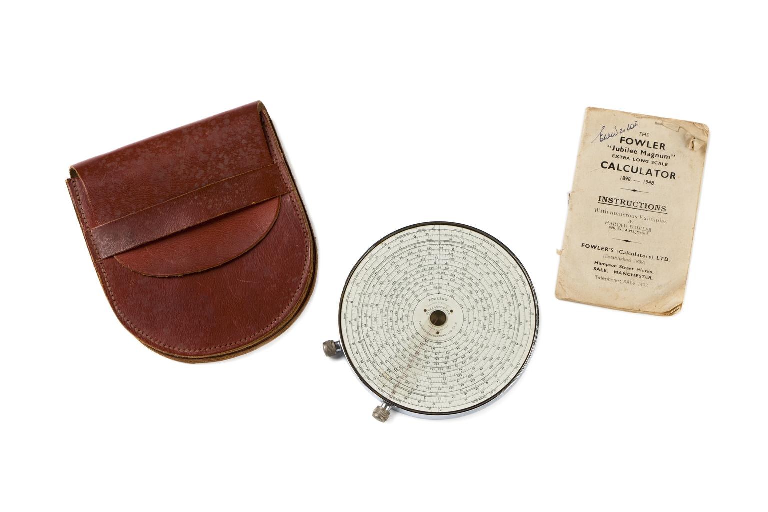 Figure 5 — A Fowler Jubilee Magnum calculator lying beside its brown leather case with a fold-over flap and its instruction booklet.